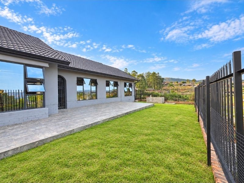 Rear view of the property featuring a spacious tiled patio, well-maintained lawn, and secure perimeter fencing with a built-in braai area.