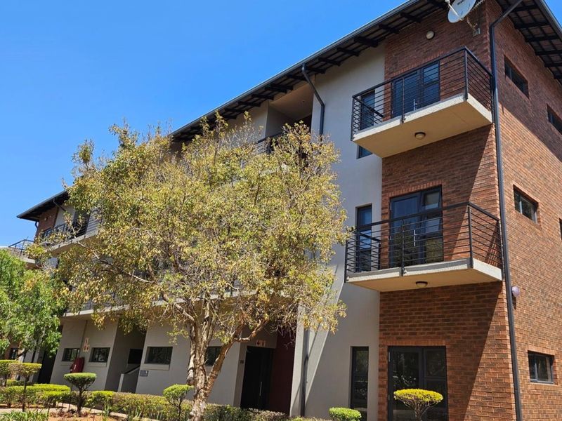 A multi-story office building featuring a brick and plaster facade, private balconies with metal railings, and well-maintained landscaped garden areas.