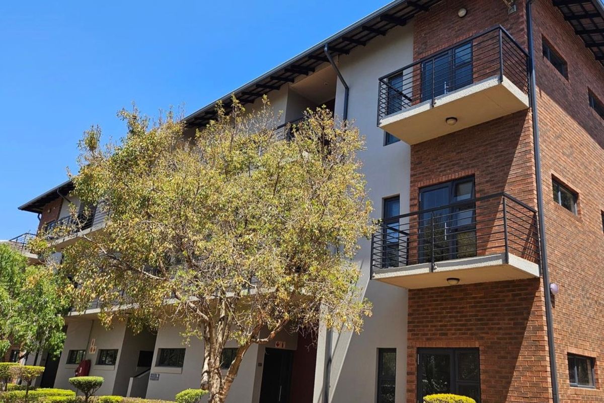 A multi-story office building featuring a brick and plaster facade, private balconies with metal railings, and well-maintained landscaped garden areas.