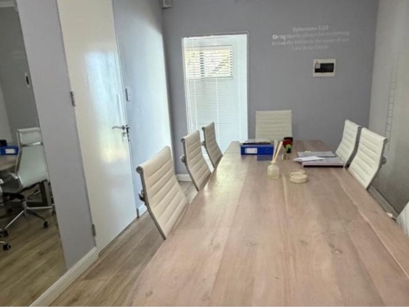 A professional office meeting room featuring light wood-look laminate flooring, a large wall mirror, and venetian blinds for natural light control.