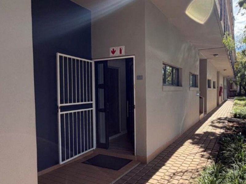 Exterior view of an office entrance featuring a security gate, paved walkway, and well-maintained building facade.