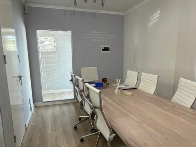 A professional office space featuring laminate flooring, neutral wall tones, and natural light provided by large windows with fitted venetian blinds.