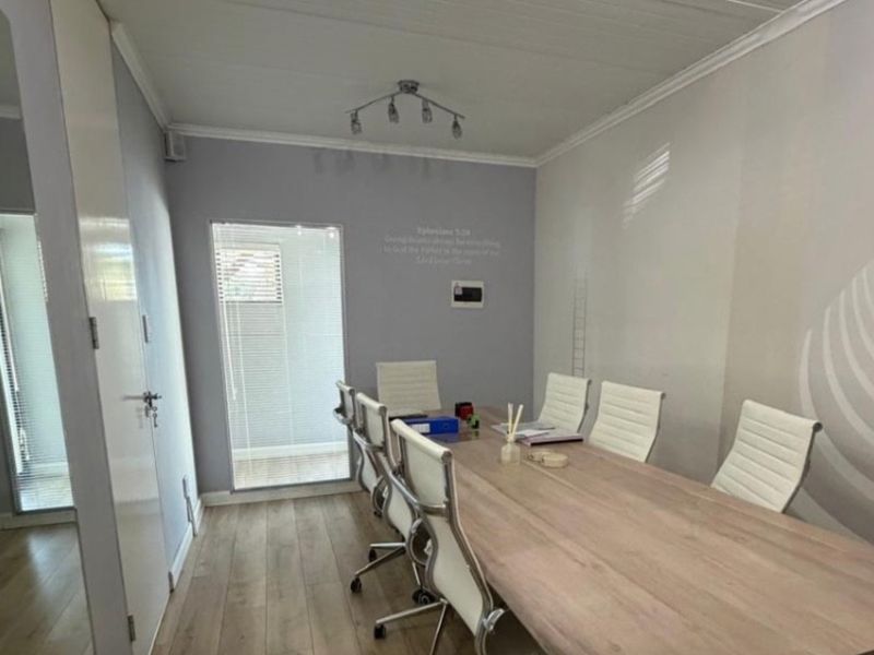 A functional office meeting room featuring laminate flooring, neutral wall tones, and natural light provided by window blinds.