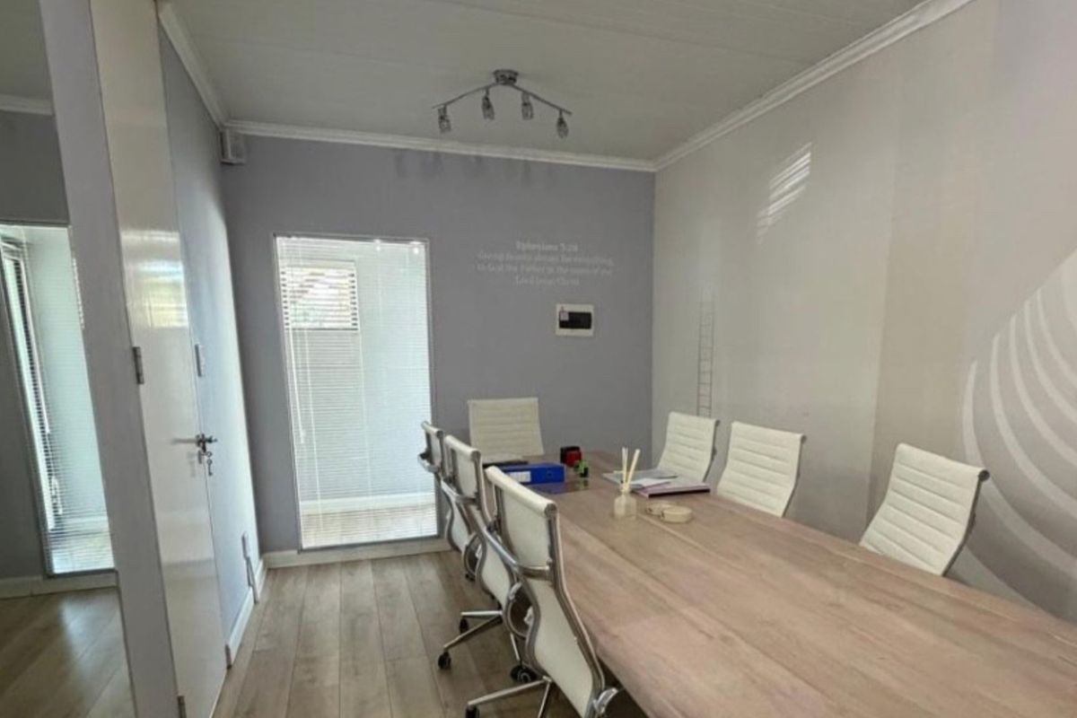 A functional office meeting room featuring laminate flooring, neutral wall tones, and natural light provided by window blinds.