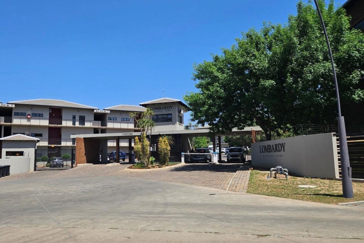 Front entrance view of Lombardy Business Park featuring a paved driveway, security boom gate, and professional signage.