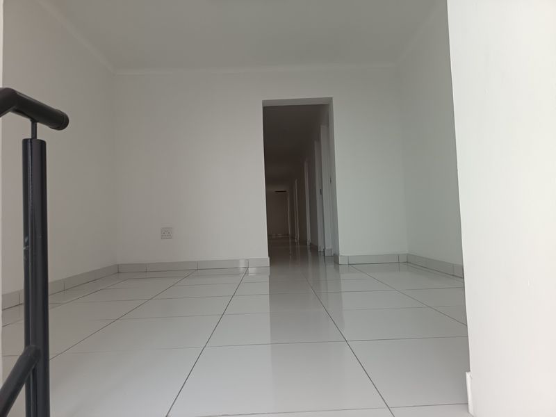 A clean, empty hallway featuring white walls, tiled flooring, and a metal handrail leading towards a corridor.