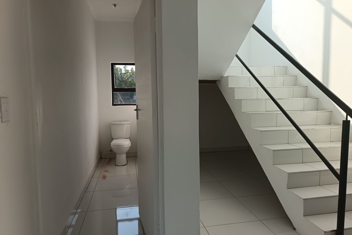 A minimalist bathroom area featuring a toilet, adjacent to a tiled staircase with a metal handrail in an industrial-style space.