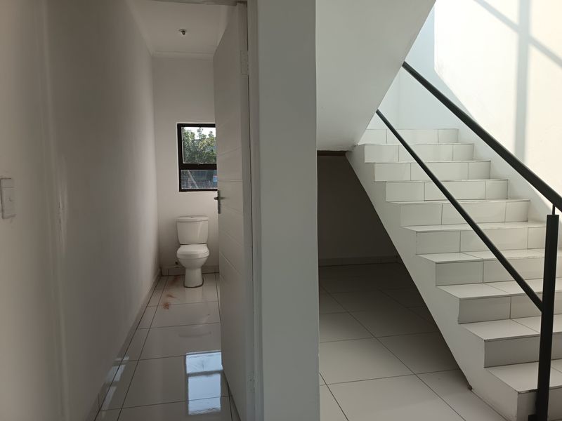 A minimalist bathroom area featuring a toilet, adjacent to a tiled staircase with a metal handrail in an industrial-style space.