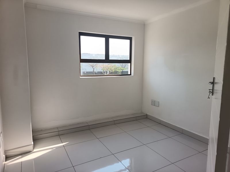 A clean, empty office space featuring white walls, tiled flooring, and a window providing natural light.