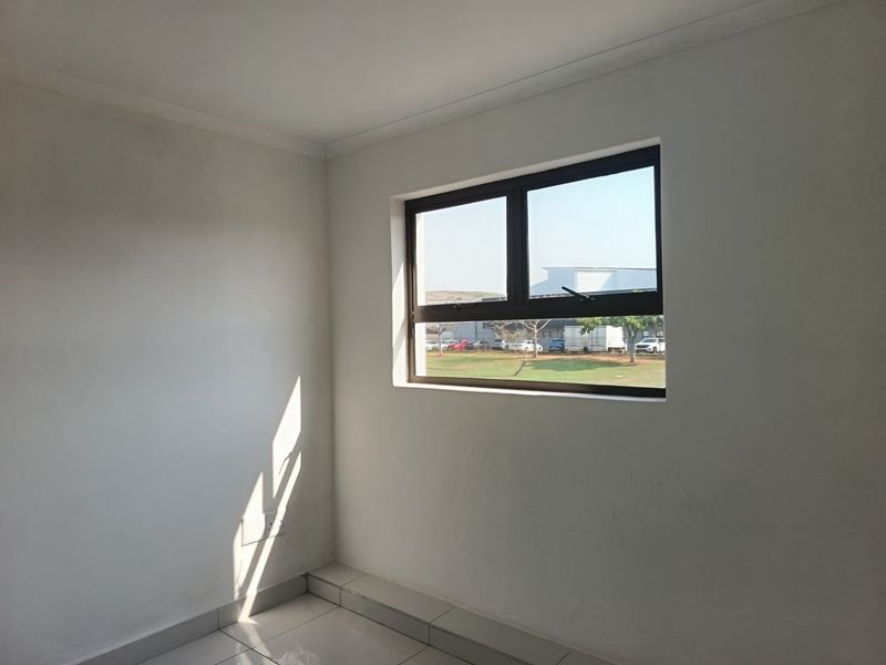 A clean, empty office space featuring neutral tiled flooring and a modern aluminium-framed window providing natural light.