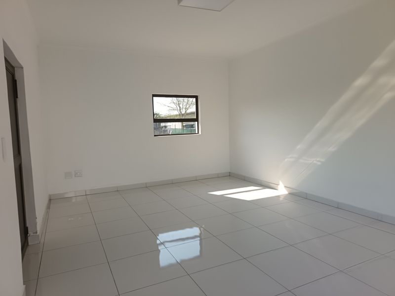 A bright, empty bedroom featuring clean white walls, polished tiled flooring, and a window allowing natural light to fill the space.