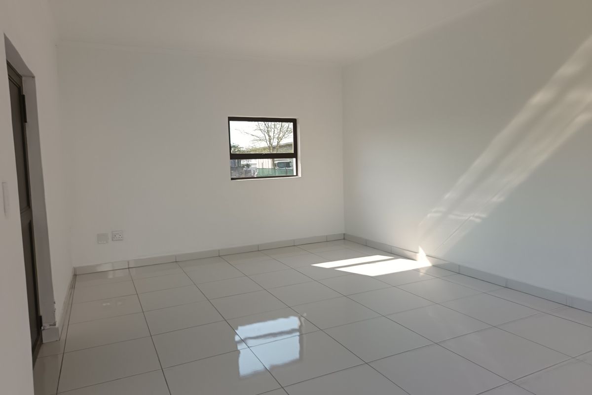A bright, empty bedroom featuring clean white walls, polished tiled flooring, and a window allowing natural light to fill the space.