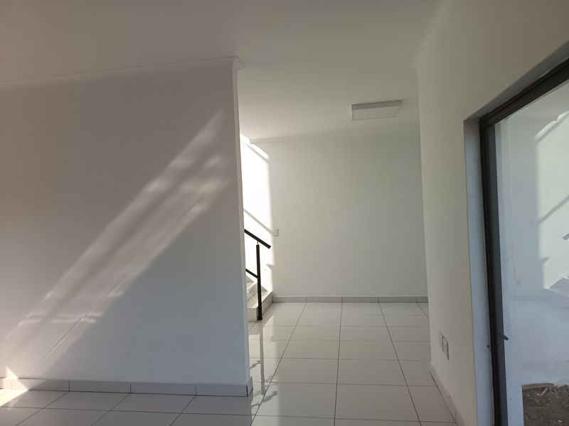 A bright, empty hallway featuring clean tiled flooring and a staircase with a modern metal railing, leading towards an exterior sliding glass door.