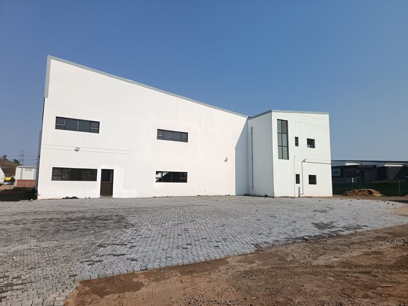 Rear view of a modern industrial building featuring a large paved yard area and clean white facade.