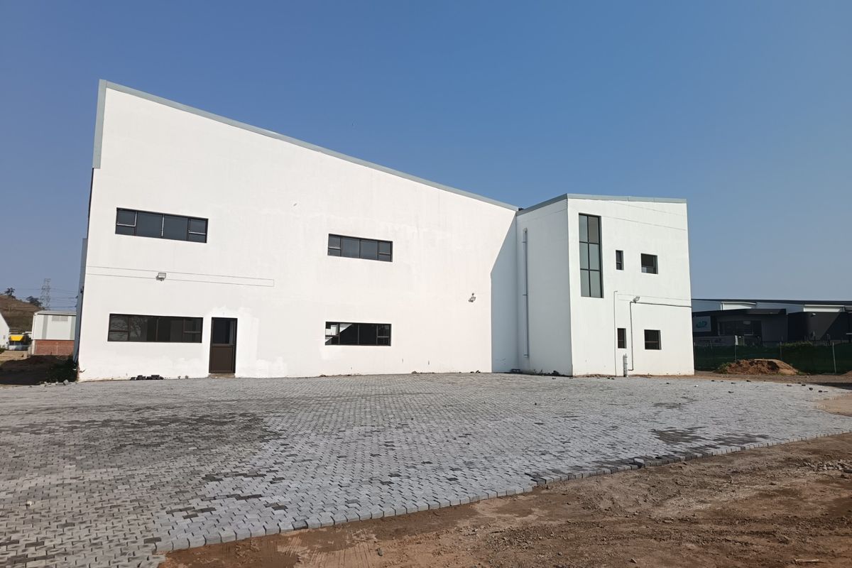 Rear view of a modern industrial building featuring a large paved yard area and clean white facade.