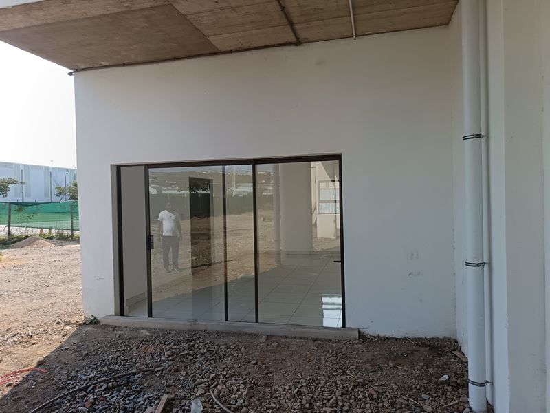 Exterior view of an industrial unit featuring a sliding glass door entrance, tiled interior flooring, and an unfinished outdoor ground area.
