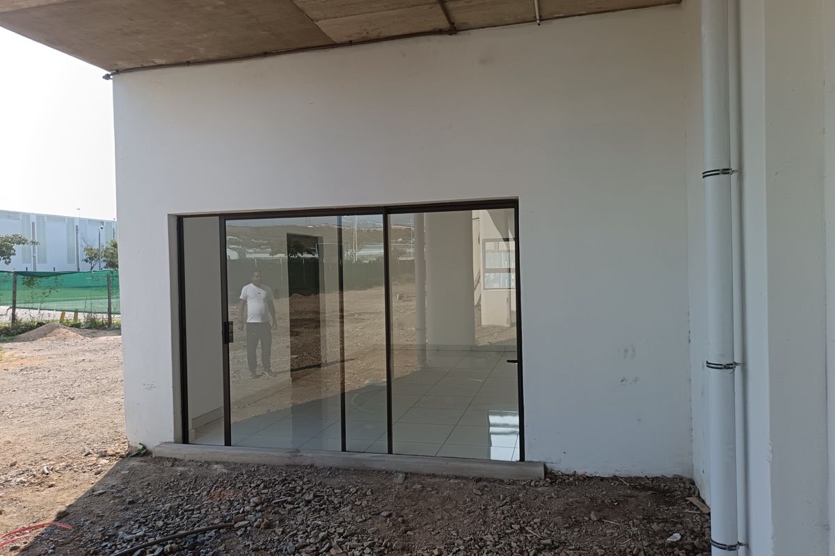 Exterior view of an industrial unit featuring a sliding glass door entrance, tiled interior flooring, and an unfinished outdoor ground area.