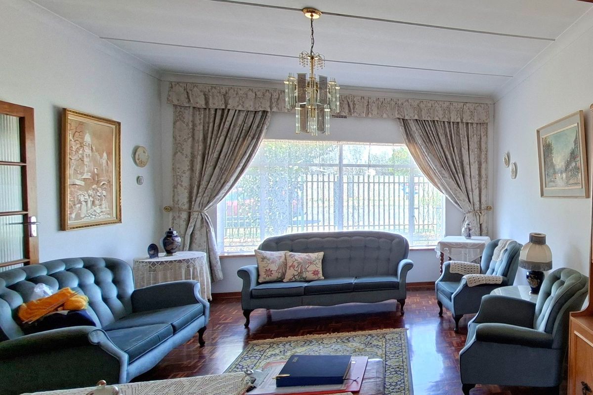 A traditional living room featuring polished parquet flooring, a classic crystal chandelier, and a large window providing natural light.