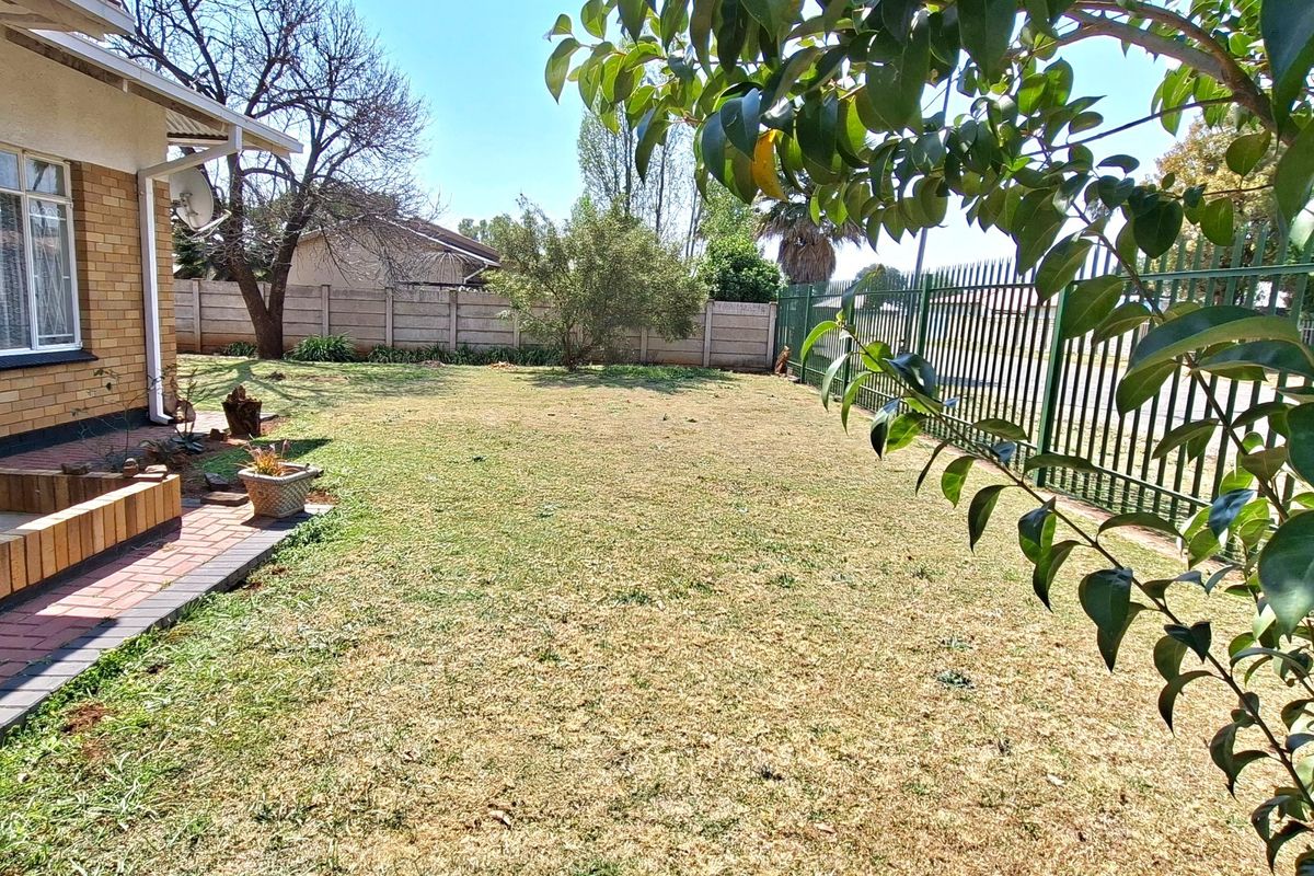 A spacious rear garden featuring a brick exterior wall, paved walkway, and secure perimeter fencing with a lawn area.