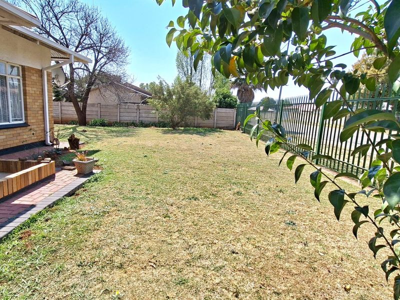 A spacious rear garden featuring a brick exterior wall, paved walkway, and secure perimeter fencing with a lawn area.