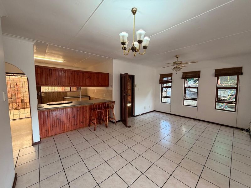 Spacious open-plan living and kitchen area featuring tiled flooring, a breakfast bar, and traditional wooden cabinetry, offering a functional layout ready for modern updates.