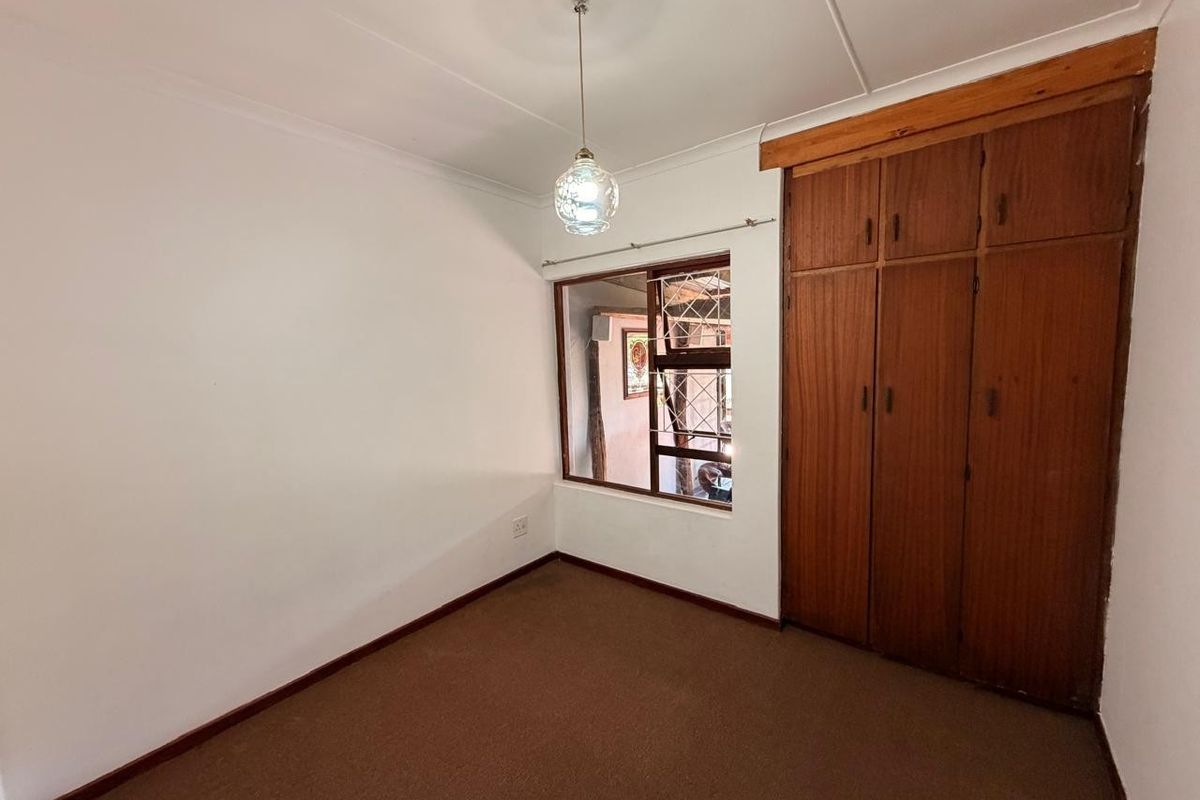 A vacant bedroom featuring built-in wooden cupboards, carpeted flooring, and a window with security bars.