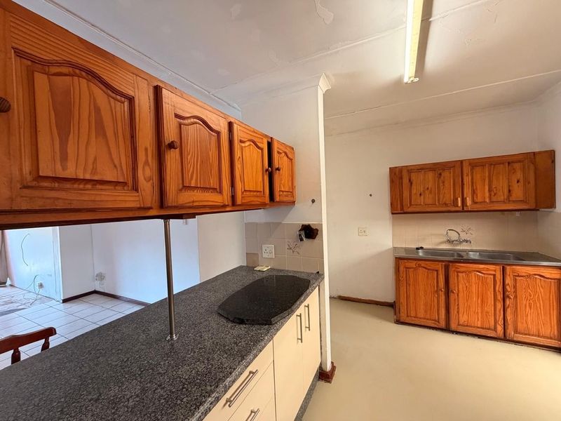 A dated kitchen featuring wooden cabinetry, granite countertops, and a double basin sink, requiring cosmetic updates to modernize the space.