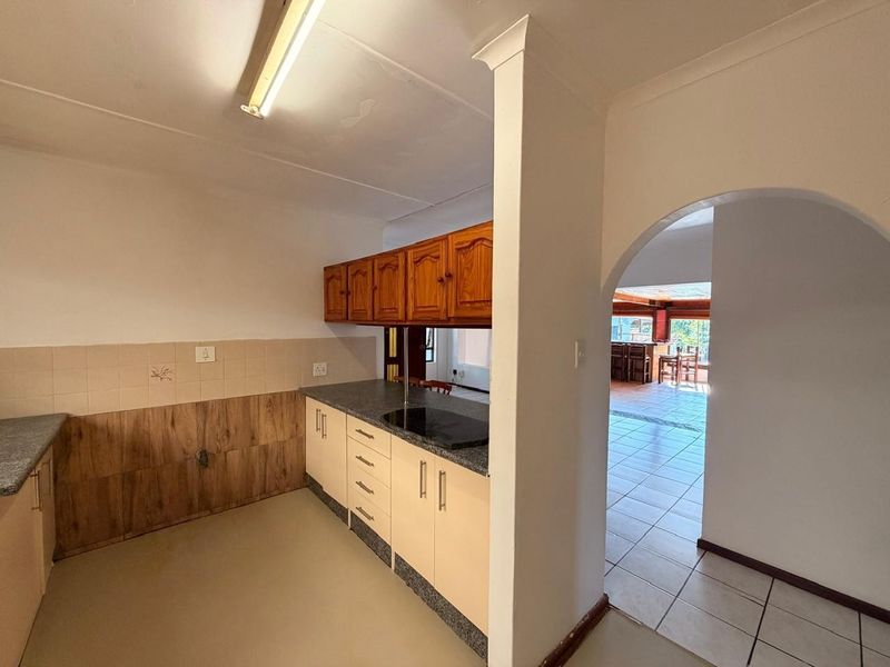 A functional kitchen space featuring built-in cabinetry, laminate countertops, and a tiled backsplash, leading through an archway into an adjacent living area.