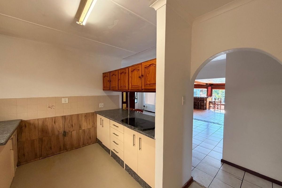 A functional kitchen space featuring built-in cabinetry, laminate countertops, and a tiled backsplash, leading through an archway into an adjacent living area.