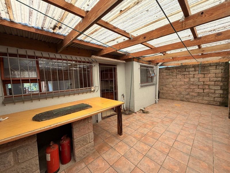 Covered outdoor patio area featuring a built-in brick counter, tiled flooring, and a corrugated roof structure, suitable for an entertainment space.