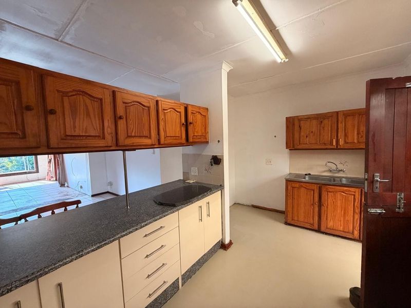 A dated kitchen featuring wooden cabinetry, granite countertops, and a stainless steel sink, requiring cosmetic updates to modernize the space.