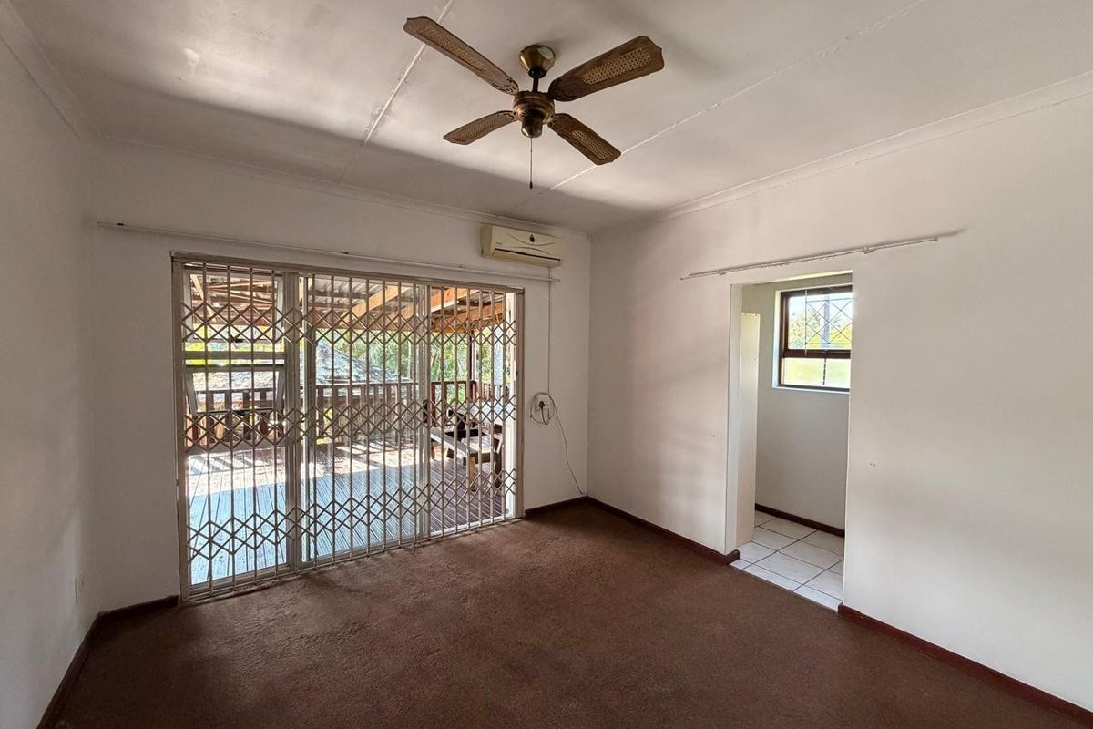 An empty living room featuring a ceiling fan, split-system air conditioner, and sliding glass doors with security gates leading to an outdoor patio area.