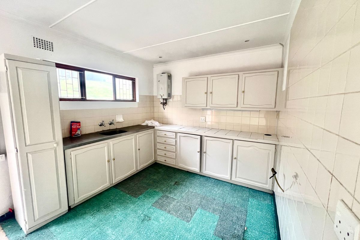 A functional kitchen space featuring built-in cabinetry, tiled splashbacks, and a gas geyser, offering a blank canvas for potential renovation and modernization.
