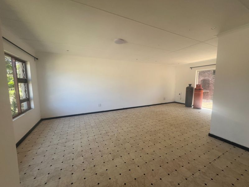 A spacious, empty living area featuring tiled flooring, recessed ceiling lighting, and large windows providing natural light.