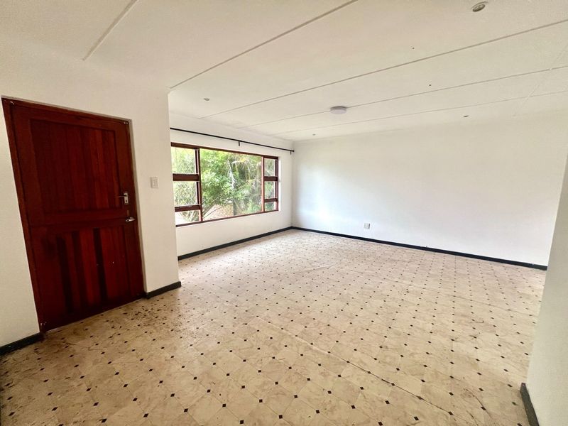 A spacious, empty living area featuring neutral walls, patterned vinyl flooring, and large windows providing natural light.