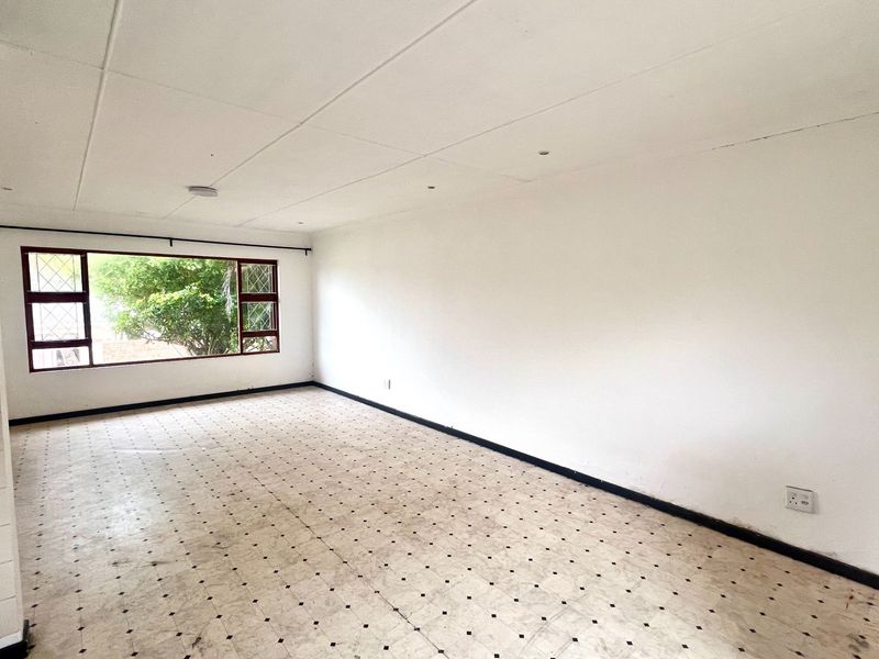 A spacious, empty living area featuring large windows and original tiled flooring, offering a blank canvas for renovation and interior design updates.