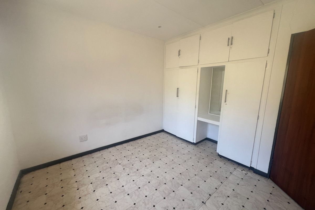 An empty bedroom featuring built-in white cupboards with an integrated vanity nook and classic patterned vinyl flooring.