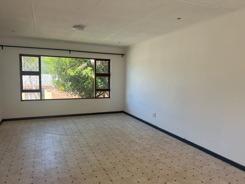 A spacious, empty living room featuring large windows, tiled flooring, and recessed ceiling lighting, offering a blank canvas for potential interior design updates.