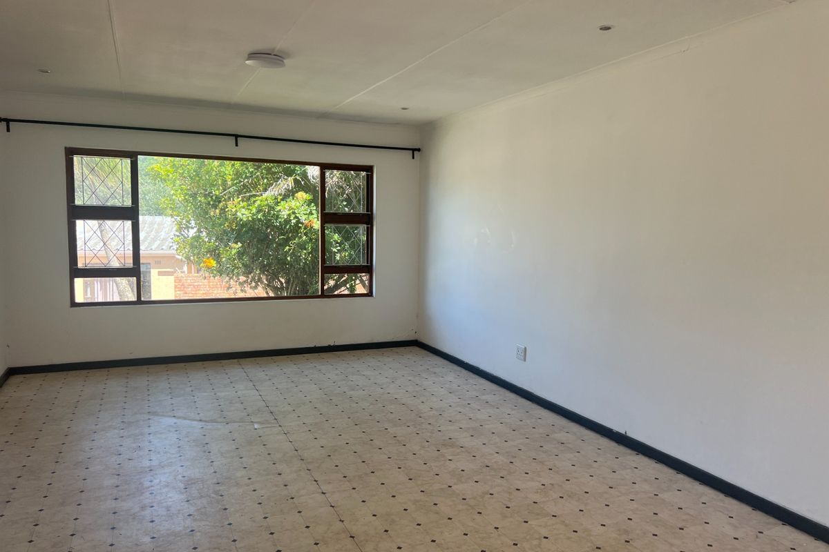A spacious, empty living room featuring large windows, tiled flooring, and recessed ceiling lighting, offering a blank canvas for potential interior design updates.