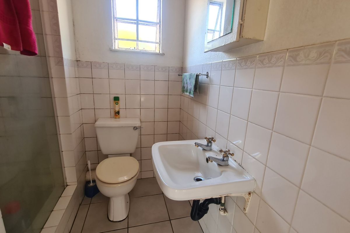 A functional bathroom featuring a wall-mounted basin, shower enclosure, and tiled finishes, currently showing signs of wear and dated fixtures.