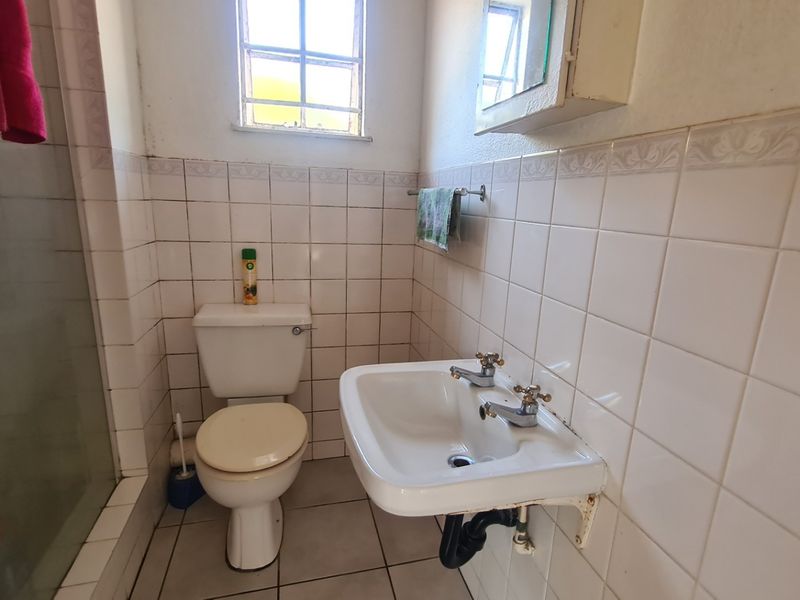 A functional bathroom featuring a wall-mounted basin, shower enclosure, and tiled finishes, currently showing signs of wear and dated fixtures.