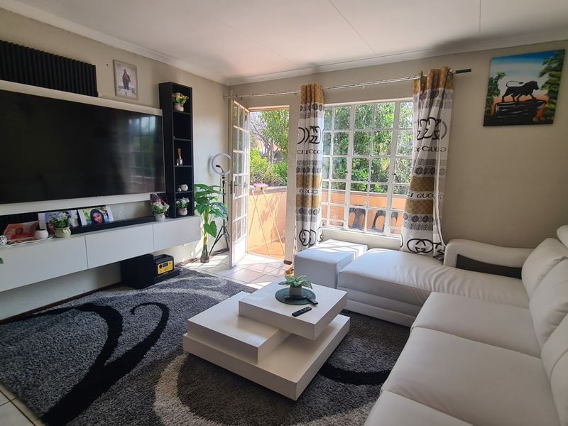 A well-maintained living room featuring tiled flooring, a built-in media console, and direct access to an outdoor balcony through a glass-paned door.