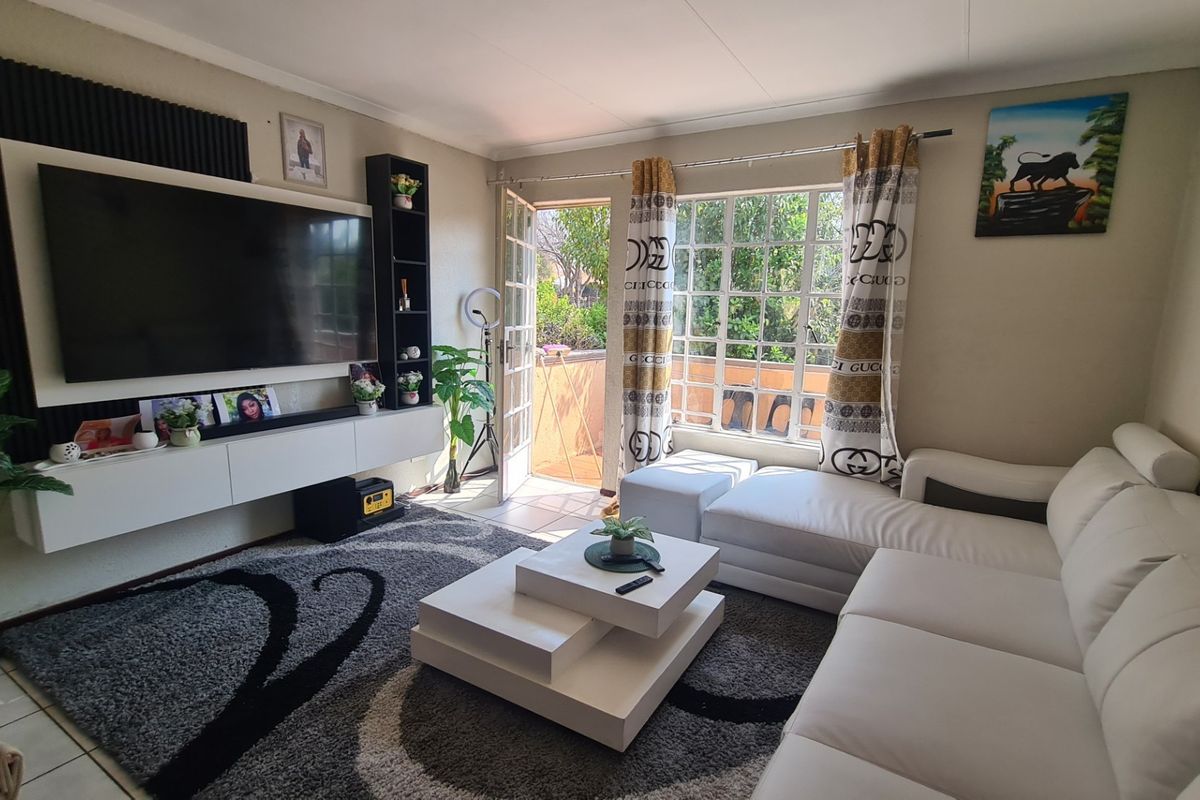 A well-maintained living room featuring tiled flooring, a built-in media console, and direct access to an outdoor balcony through a glass-paned door.