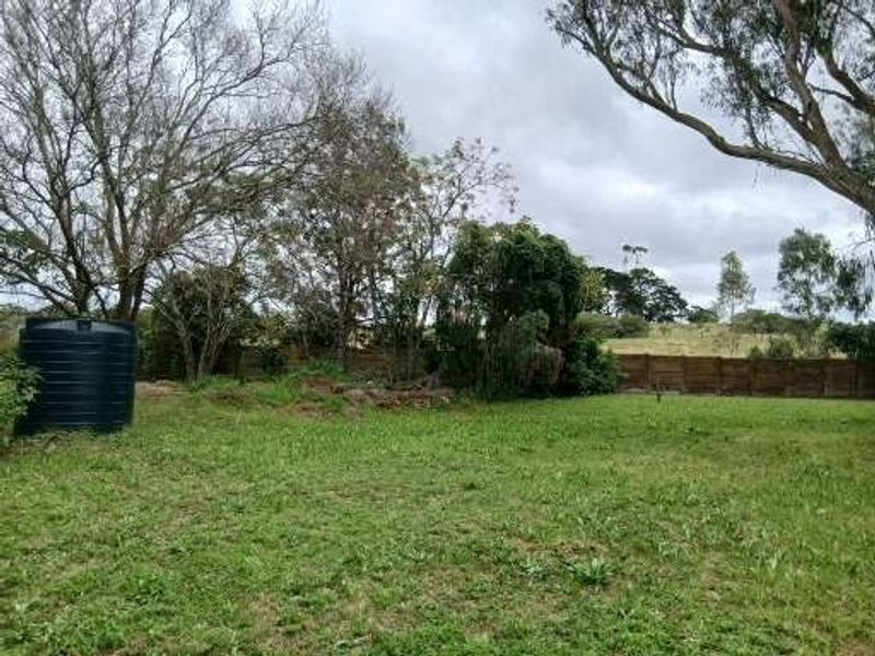Expansive garden area featuring mature trees, timber boundary fencing, and a large water storage tank on the property grounds.