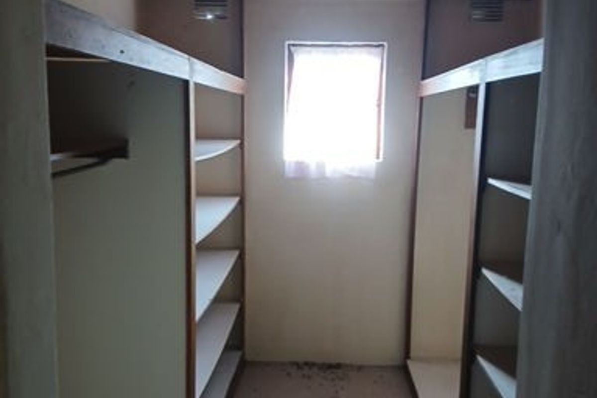 A walk-in closet or dressing area featuring built-in shelving units, a timber-clad ceiling, and a central window for natural light.