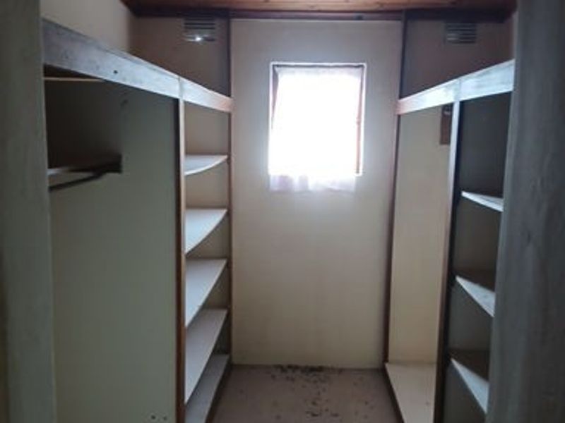 A walk-in closet or dressing area featuring built-in shelving units, a timber-clad ceiling, and a central window for natural light.