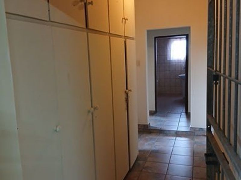A functional hallway featuring extensive built-in storage cupboards, tiled flooring, and a timber-clad ceiling, leading through to an adjacent room.