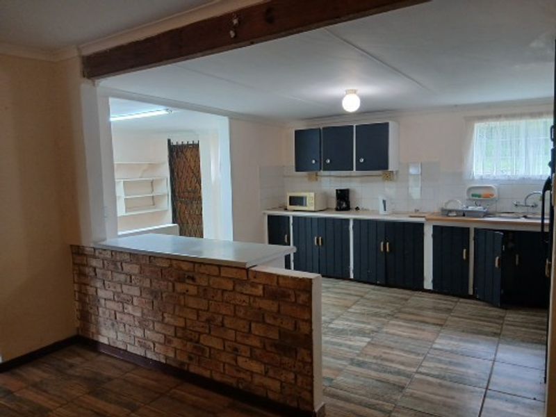 Open plan kitchen featuring a rustic brick breakfast bar, tiled flooring, and ample built-in cabinetry, connecting to a secondary utility or pantry area.