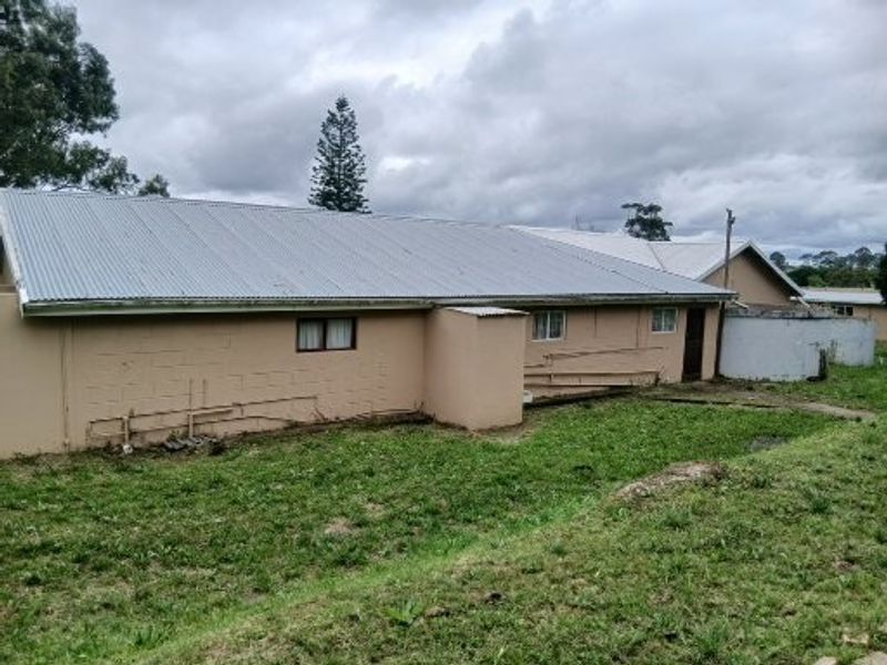 Rear view of the property showing corrugated metal roofing, concrete block construction, and an external water storage tank on a grassed plot.