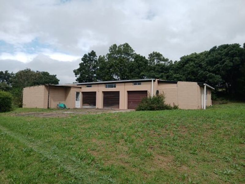 A detached multi-car garage building with three garage doors, situated on a large grassy plot with mature trees in the background.